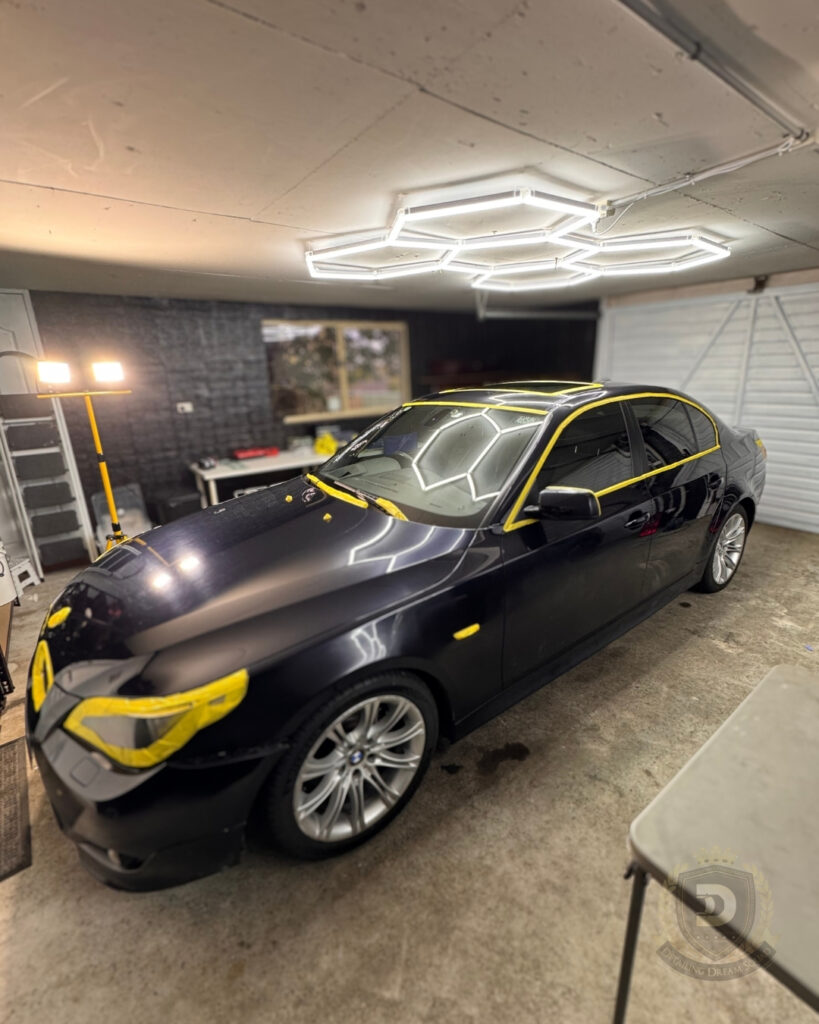 Black BMW sedan masked with yellow tape under professional detailing lights for paint correction and graphene coating preparation at Detailing Dream Squad in Sydney
