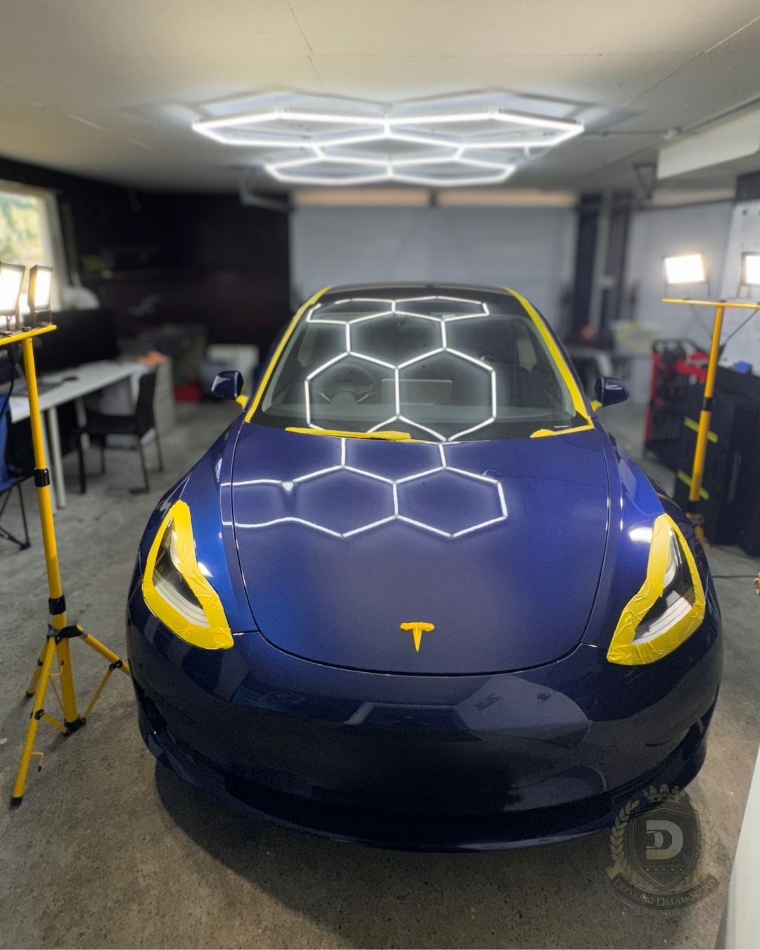Blue Tesla with yellow masking tape under hexagon detailing lights and inspection stands in Detailing Dream Squad studio for paint correction preparation in Sydney