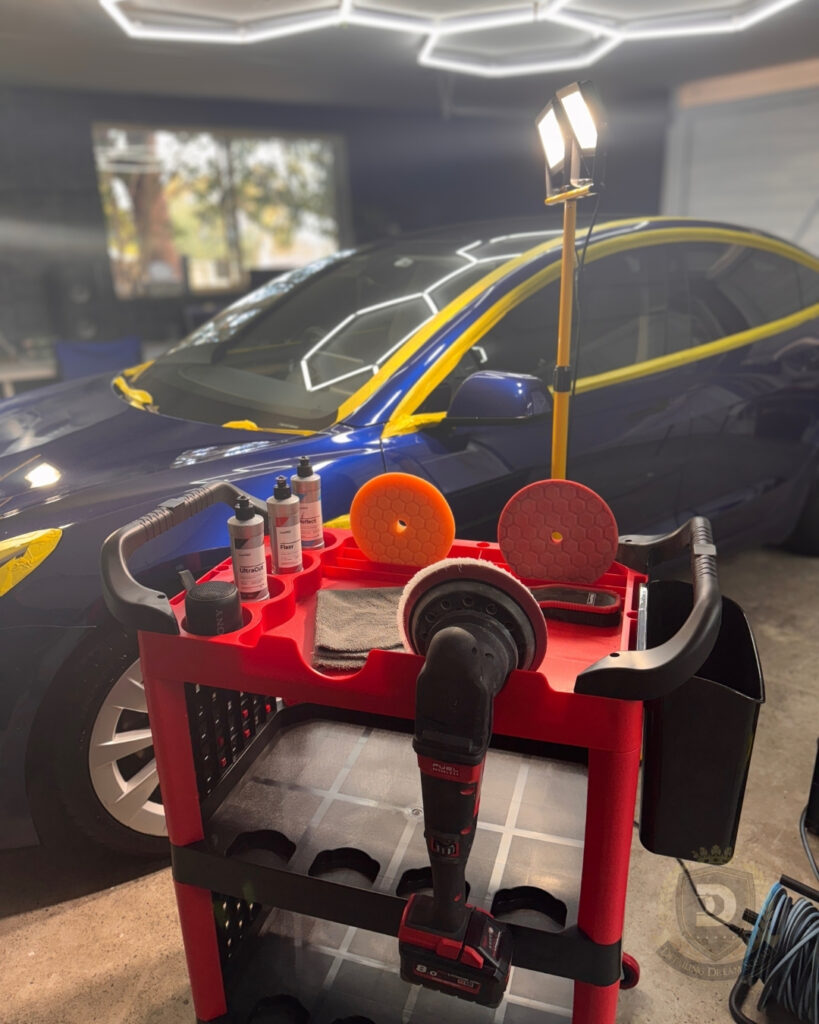 Paint correction setup with polishing machine, pads and products in front of blue Tesla taped for detailing before ceramic coating at Detailing Dream Squad in Sydney