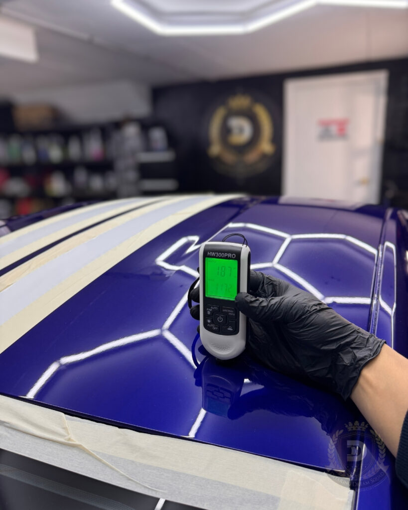 Detailing Dream Squad technician using paint thickness gauge on blue car roof under inspection lights to ensure safe professional polishing in Sydney