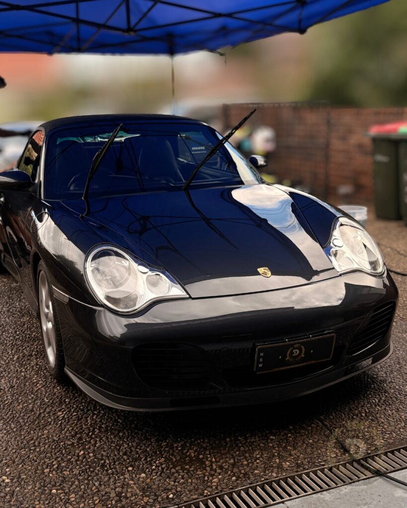 Black Porsche sports car detailed and polished to high gloss under mobile canopy by Detailing Dream Squad ceramic coating specialists in Sydney